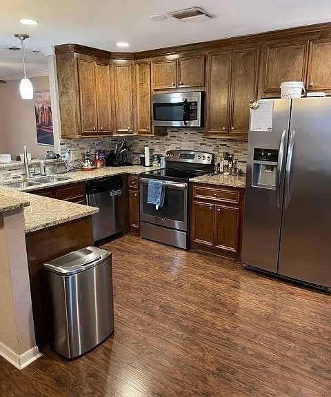 kitchen with tasteful backsplash, visible vents, light stone counters, appliances with stainless steel finishes, and a peninsula