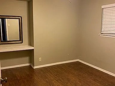 spare room featuring baseboards and dark wood-style flooring