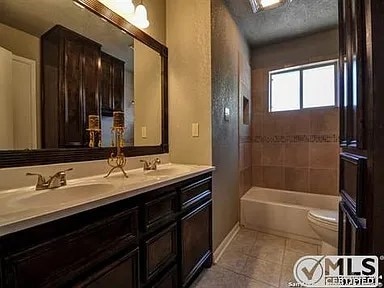 bathroom with toilet, a sink, a textured ceiling, tile patterned flooring, and double vanity