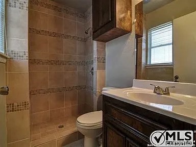 full bath with tiled shower, toilet, and vanity