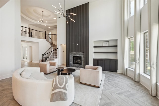 living room featuring stairs, a high ceiling, baseboards, and a chandelier