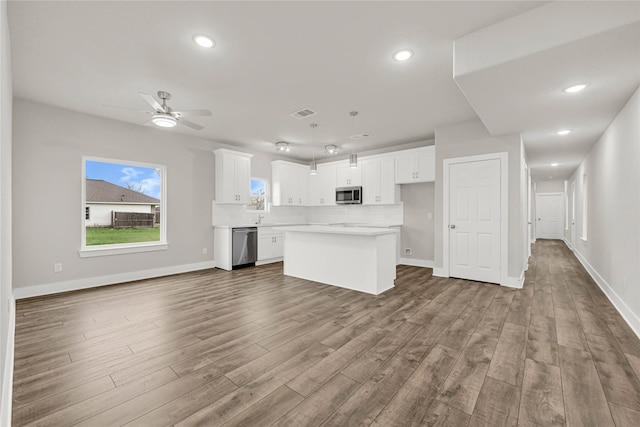 kitchen featuring wood finished floors, a kitchen island, white cabinets, appliances with stainless steel finishes, and backsplash