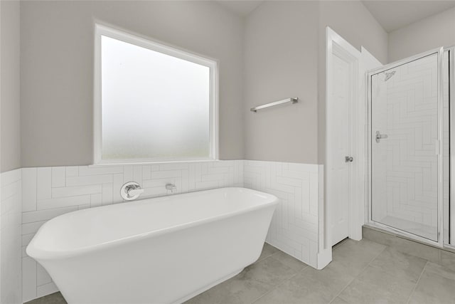 bathroom featuring a freestanding tub, a shower stall, wainscoting, tile walls, and tile patterned floors