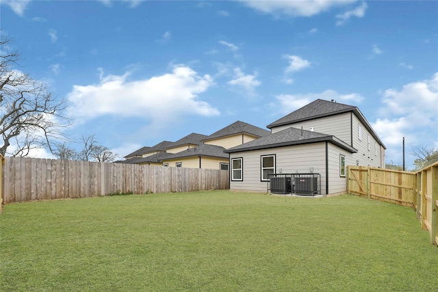 back of house featuring a yard, roof with shingles, central AC, and a fenced backyard