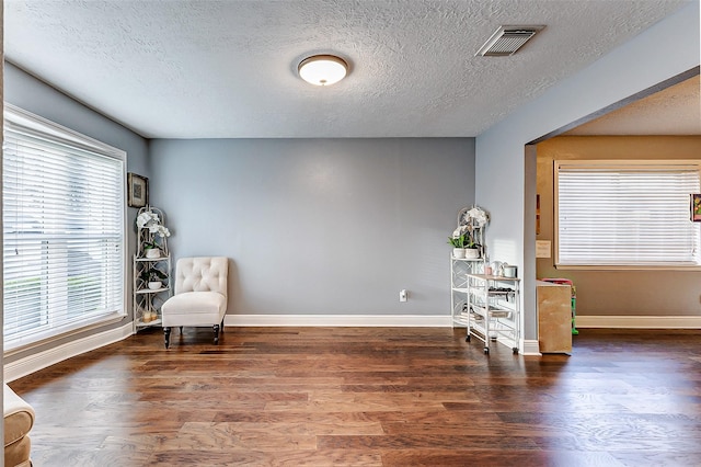 living area with a textured ceiling, wood finished floors, visible vents, and baseboards