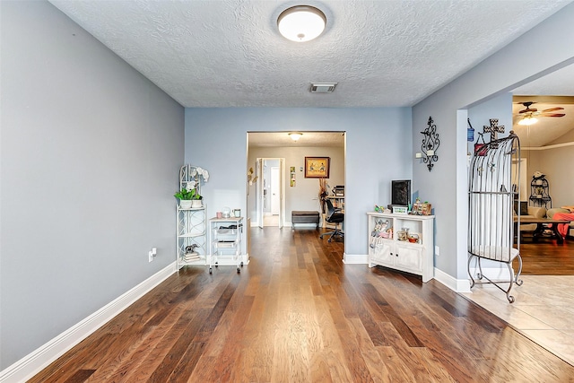 corridor featuring visible vents, a textured ceiling, baseboards, and wood finished floors