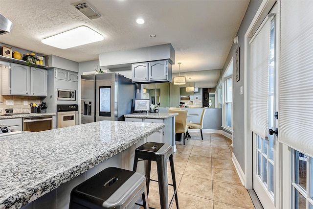 kitchen featuring light tile patterned floors, visible vents, a peninsula, appliances with stainless steel finishes, and backsplash