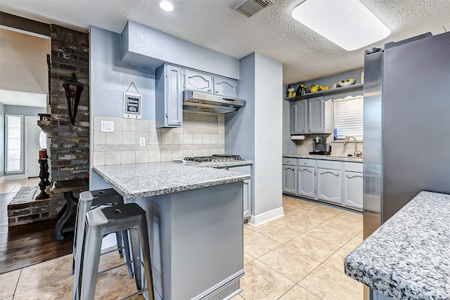 kitchen featuring visible vents, under cabinet range hood, a peninsula, freestanding refrigerator, and light tile patterned flooring