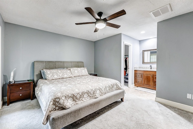 bedroom with baseboards, visible vents, a sink, light carpet, and a walk in closet