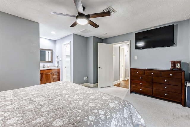 bedroom with visible vents, a textured ceiling, ensuite bath, baseboards, and light colored carpet