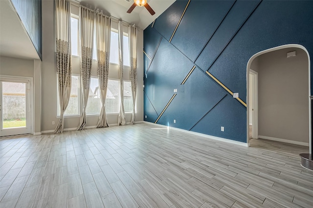 empty room featuring a wealth of natural light, wood finish floors, arched walkways, and a ceiling fan