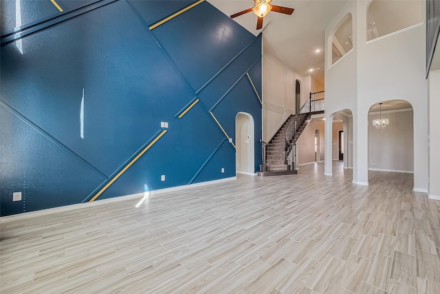 unfurnished living room with ceiling fan with notable chandelier, wood finished floors, stairway, arched walkways, and a high ceiling