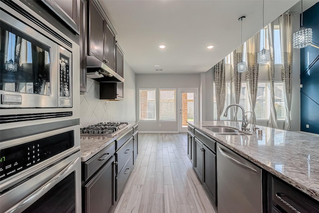 kitchen with a sink, light stone counters, under cabinet range hood, backsplash, and stainless steel appliances