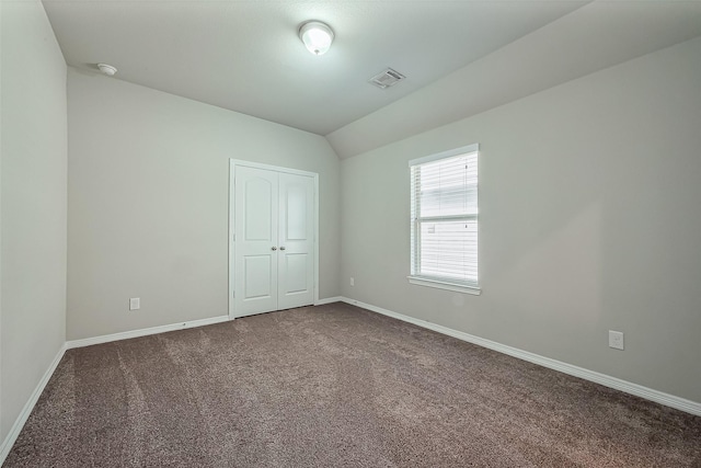 spare room featuring visible vents, dark colored carpet, baseboards, and vaulted ceiling