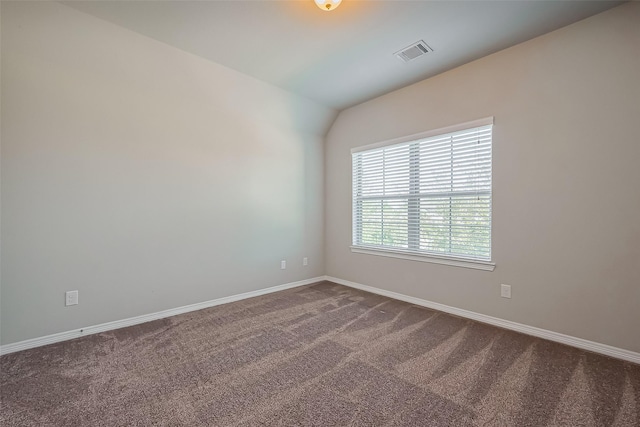 spare room with dark colored carpet, visible vents, baseboards, and lofted ceiling