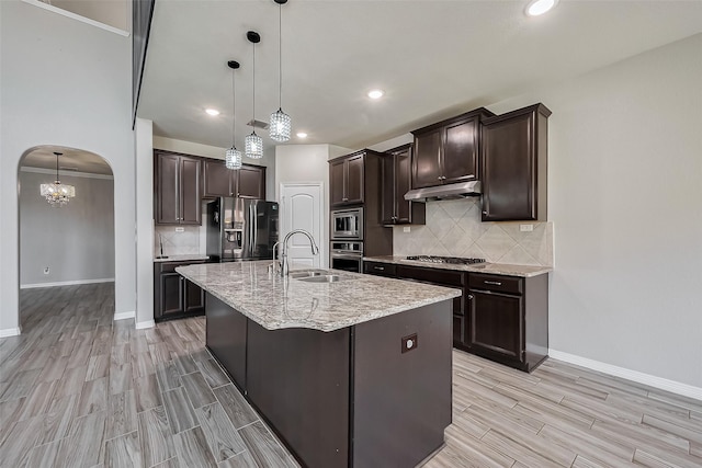 kitchen with dark brown cabinetry, under cabinet range hood, appliances with stainless steel finishes, arched walkways, and a sink