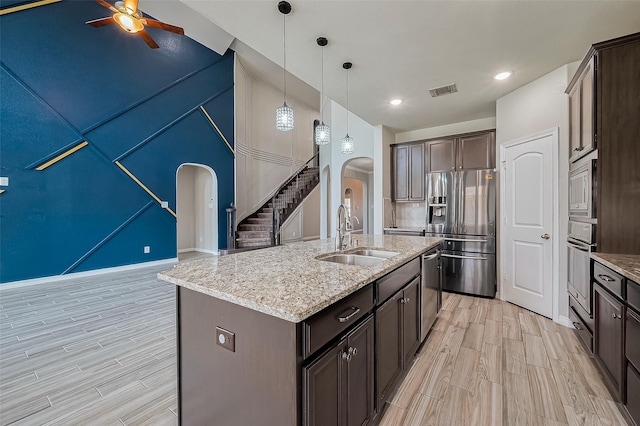 kitchen with ceiling fan, dark brown cabinetry, appliances with stainless steel finishes, arched walkways, and a sink