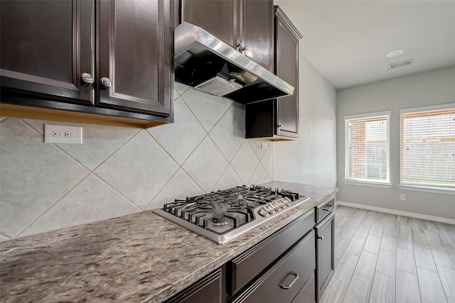 kitchen featuring extractor fan, stainless steel gas stovetop, dark brown cabinets, and tasteful backsplash