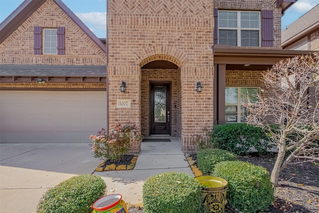 doorway to property with concrete driveway, a garage, and brick siding