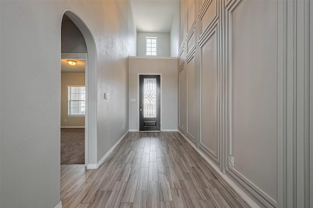 foyer entrance featuring a wealth of natural light, baseboards, arched walkways, and wood finished floors