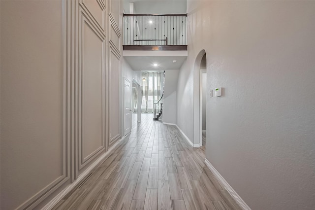 hall with light wood finished floors, arched walkways, a high ceiling, and baseboards