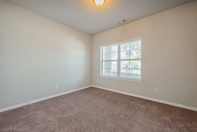 spare room featuring dark colored carpet, visible vents, and baseboards