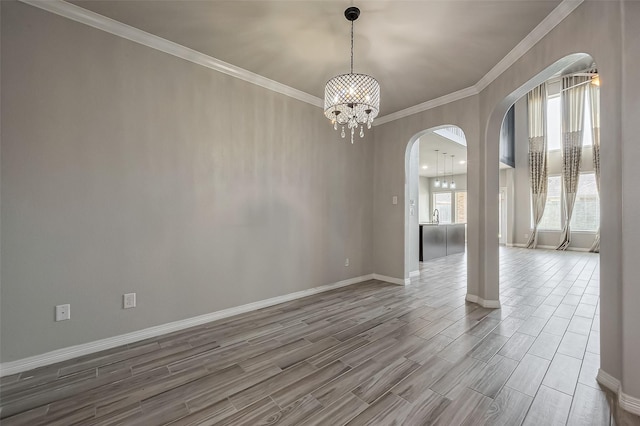 empty room featuring wood finish floors, a notable chandelier, ornamental molding, arched walkways, and baseboards