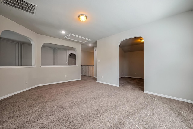 spare room with visible vents, carpet floors, arched walkways, baseboards, and attic access