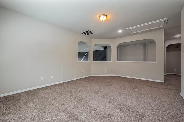 carpeted spare room with visible vents, attic access, and baseboards