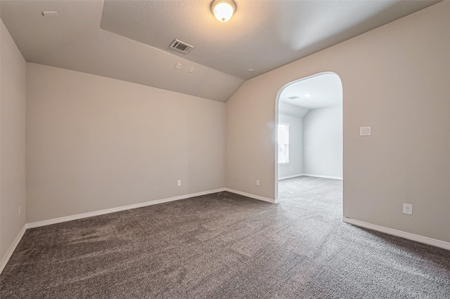 empty room with visible vents, arched walkways, carpet flooring, baseboards, and vaulted ceiling