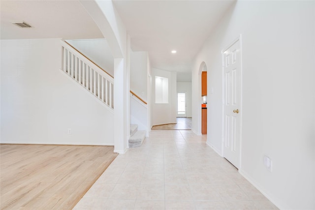 foyer featuring visible vents, baseboards, stairs, light tile patterned floors, and arched walkways