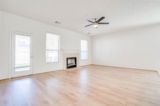 unfurnished living room with a ceiling fan, visible vents, light wood finished floors, and a tile fireplace