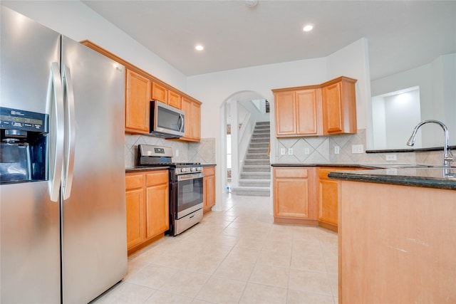 kitchen with light tile patterned floors, stainless steel appliances, arched walkways, and backsplash