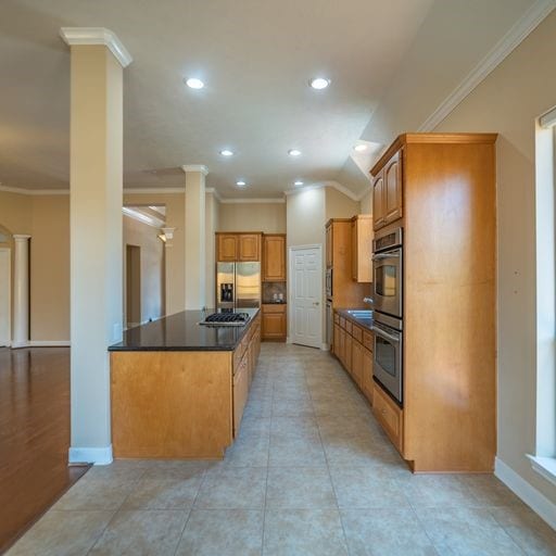 kitchen with baseboards, decorative columns, ornamental molding, stainless steel appliances, and dark countertops