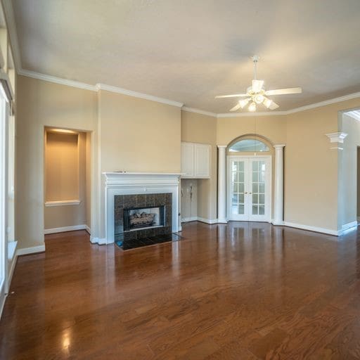 unfurnished living room with french doors, wood finished floors, ceiling fan, and a tiled fireplace