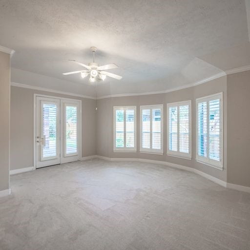 empty room featuring a ceiling fan, a textured ceiling, carpet floors, crown molding, and baseboards