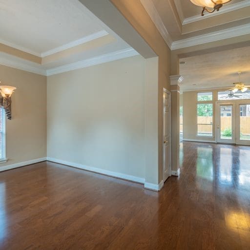 empty room with a raised ceiling, ornamental molding, ceiling fan with notable chandelier, wood finished floors, and baseboards