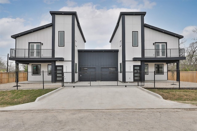 view of front facade featuring a fenced front yard, french doors, concrete driveway, and a balcony