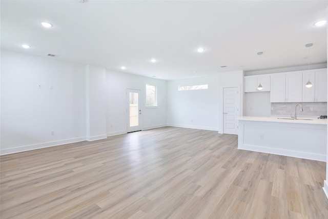 unfurnished living room featuring recessed lighting, light wood finished floors, baseboards, and a sink