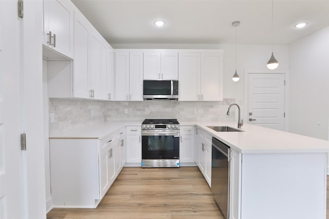 kitchen with white cabinets, light countertops, a sink, a peninsula, and appliances with stainless steel finishes