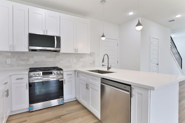 kitchen featuring visible vents, a peninsula, light wood-style flooring, a sink, and stainless steel appliances