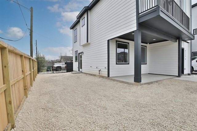 view of home's exterior with gravel driveway, fence, a patio area, and a balcony