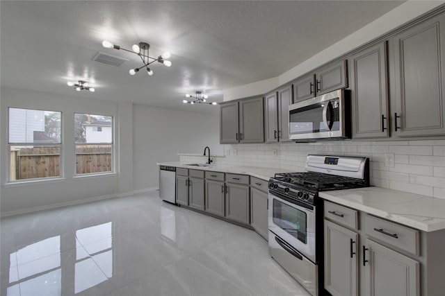 kitchen featuring tasteful backsplash, visible vents, gray cabinets, appliances with stainless steel finishes, and a sink