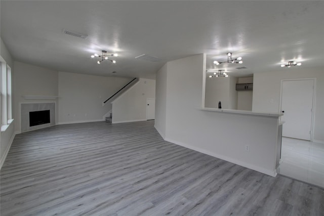 unfurnished living room with visible vents, stairway, light wood-style flooring, a fireplace, and a notable chandelier