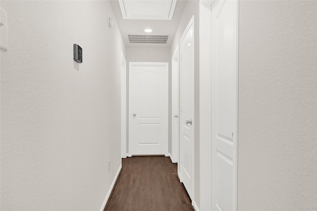 hallway featuring dark wood-style floors, visible vents, attic access, and baseboards