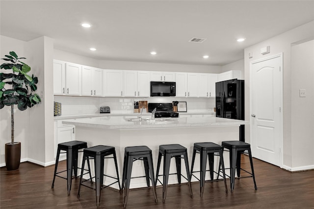 kitchen featuring visible vents, white cabinetry, black appliances, and a kitchen breakfast bar