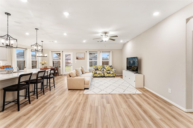 living room featuring light wood finished floors, recessed lighting, ceiling fan with notable chandelier, and baseboards