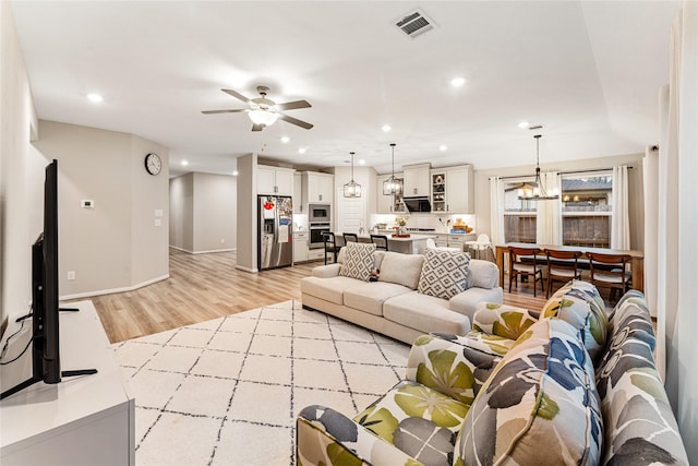 living room featuring baseboards, visible vents, recessed lighting, ceiling fan with notable chandelier, and light wood-type flooring