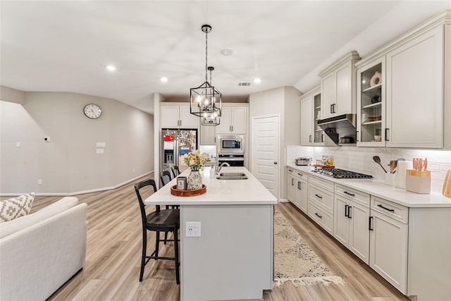 kitchen with light wood-type flooring, tasteful backsplash, appliances with stainless steel finishes, a breakfast bar area, and glass insert cabinets