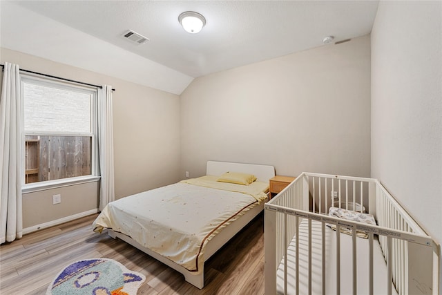 bedroom featuring vaulted ceiling, baseboards, visible vents, and light wood finished floors